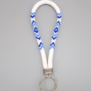 May include: White beaded key chain with a blue and light blue geometric pattern. The key chain has a silver ring and a silver clasp.