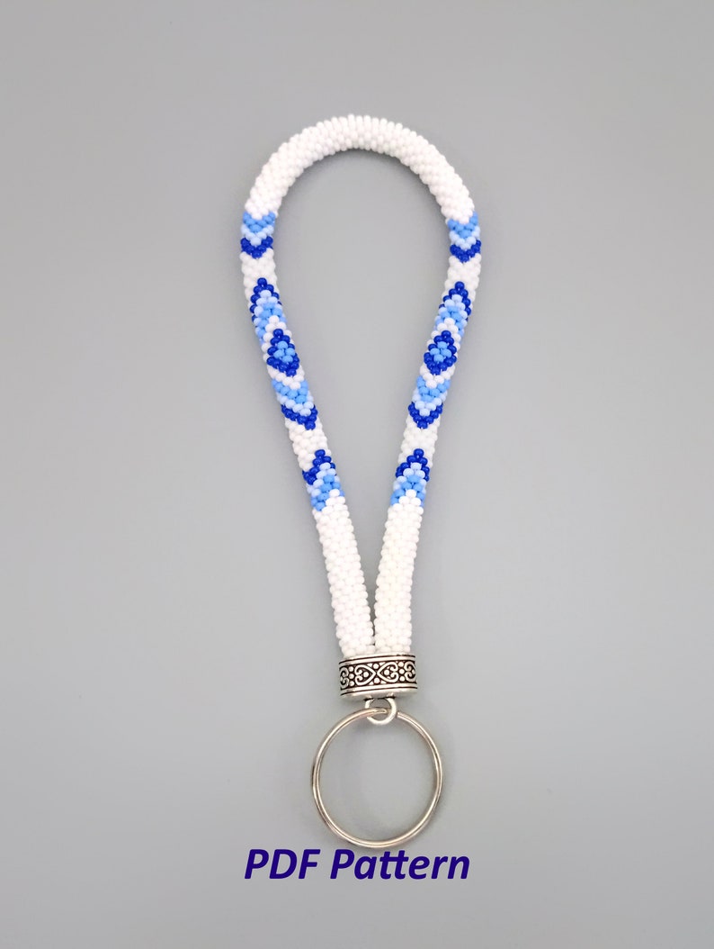 May include: White beaded key chain with a blue and light blue geometric pattern. The key chain has a silver ring and a silver clasp.