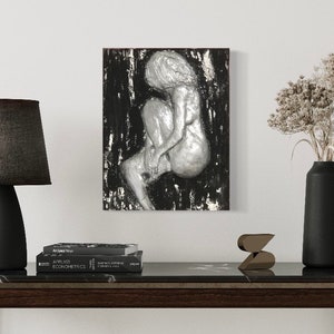 May include: A silver sculpture of a woman sitting with her legs crossed, mounted on a black and silver textured background.