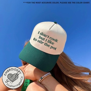 Puede incluir: Gorra de béisbol crema y verde oscuro con el texto "I don't cook but I like to stir the pot". La gorra tiene una visera verde oscuro y un botón en la parte superior. Parte de la colección Embroidery Lisa Harrington.