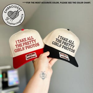May include: Two baseball caps with the text "I TAKE ALL THE PRETTY GIRLS' PHOTOS." One cap has a red brim, the other a black brim. Both caps have a white crown and a small tag on the front.