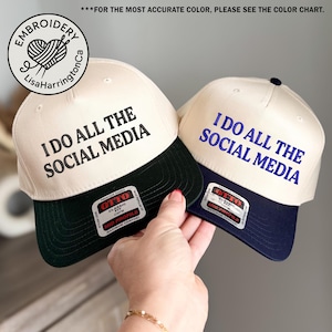 May include: Two baseball caps with the text "I DO ALL THE SOCIAL MEDIA." One cap has a black brim and text, the other has a navy blue brim and text. The caps are cream-coloured with a logo that says "Embroidery LisaHarringtonCa."