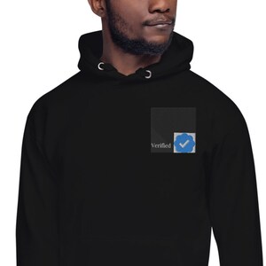May include: Black hoodie with a small square patch on the left chest. The patch has a white background with the word "Verified" and a blue checkmark icon.