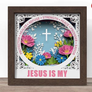 Könnte beinhalten: Ein gerahmtes Papierkunstwerk mit einem braunen Holzrahmen. Das Kunstwerk zeigt ein weißes Kreuz, bunte Blumen und den Text "JESUS IS MY". Ein kreisförmiges Design enthält Wörter wie "PROTECTOR" und "STRENGTH".