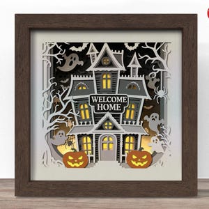 Könnte beinhalten: Ein gerahmtes Halloween-Papierkunstwerk. Das Kunstwerk zeigt ein gruseliges Spukhaus mit den Worten "WELCOME HOME" auf einem Schild. Geister, Fledermäuse, Spinnen und Kürbislaternen sind ebenfalls enthalten. Der Rahmen ist dunkelbraun.