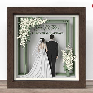 May include: A framed 3D paper art piece featuring a bride and groom. The artwork includes white floral accents and the text "You & Me Forever and Always." The frame is a dark brown color.