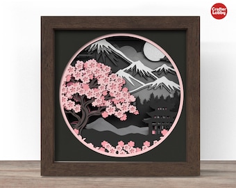 Puede incluir: Una obra de arte en papel enmarcada que presenta un diseño en capas de un paisaje japonés. La obra de arte incluye un cerezo en flor, montañas, una pagoda y una luna llena, todo en tonos de rosa, gris y negro. El marco es de color marrón oscuro.