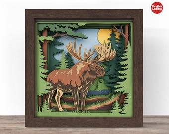 Peut inclure: Une œuvre d'art encadrée en papier représentant un élan brun avec de grands bois dans une forêt. L'œuvre utilise du papier en couches pour créer de la profondeur, avec un soleil jaune et des arbres verts. Le cadre est marron foncé, et l'œuvre est étiquetée "Crafter Lobby".
