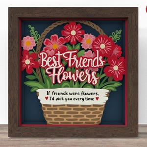 Pode incluir: Uma obra de arte emoldurada com uma moldura de madeira marrom escura. A obra apresenta uma cesta de flores vermelhas e rosas com as palavras "Best Friends Flowers" e uma citação sobre amizade.