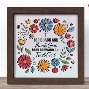 May include: A framed print with a floral wreath design. The wreath features colorful flowers in red, blue, and yellow, with green leaves. The text reads "Look Back and Thank God, Look Forward and Trust God."