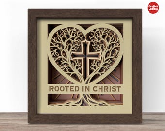 May include: A framed, layered wooden art piece featuring a heart-shaped tree design with a cross at the center. The text "ROOTED IN CHRIST" is displayed at the bottom. The frame is brown.