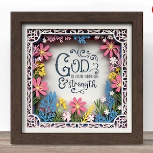 May include: A framed paper art piece with a dark brown wooden frame. The artwork features a floral design with pink, yellow, and blue paper flowers surrounding the text "GOD is our refuge & strength" in a decorative font.