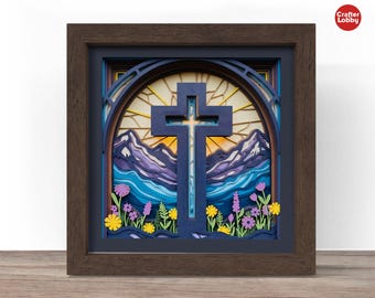 May include: A framed, layered paper art piece featuring a cross, mountains, and flowers. The cross is centered against a stained-glass style background. The artwork is in a dark brown frame, with yellow, purple, and blue hues.