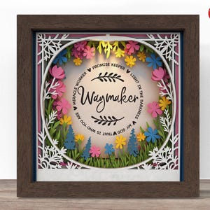 May include: A framed, layered paper art piece with a dark brown wooden frame. The artwork features a floral design with the word "Waymaker" in the center, surrounded by colorful paper flowers and the text "Miracle Worker, Promise Keeper, Light in the Darkness, My God That Is Who You Are."