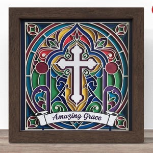 May include: A framed, layered paper art piece with a stained-glass effect. The design features a white cross at the center, surrounded by colorful geometric shapes in red, blue, green, and yellow. The words "Amazing Grace" are displayed on a banner.