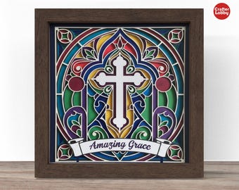 May include: A framed, layered paper art piece with a stained-glass effect. The design features a white cross at the center, surrounded by colorful geometric shapes in red, blue, green, and yellow. The words "Amazing Grace" are displayed on a banner.