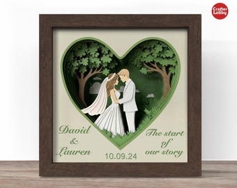 May include: A framed paper art piece featuring a couple in a heart-shaped forest scene. The artwork includes the names "David & Lauren", the date "10.09.24", and the phrase "The start of our story". The frame is brown.