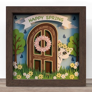 May include: A framed paper art piece with a spring theme. The artwork features a brown door with a floral wreath, a white cat wearing a flower crown, and the text "HAPPY SPRING" on a banner. Green trees, grass, and flowers complete the scene.
