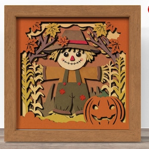 May include: A papercraft 3D wall art featuring a scarecrow with a brown hat and a pumpkin. The scarecrow is standing in a field of corn stalks and fall leaves. The background is a warm orange color.