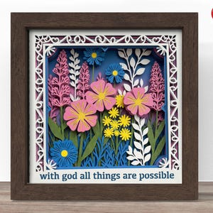 May include: A framed paper art piece featuring a layered floral design. Pink, yellow, and blue flowers are set against a blue background. The frame is dark brown, and the text "with god all things are possible" is at the bottom.
