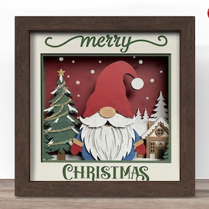 May include: A framed Christmas artwork featuring a gnome with a red hat and white beard. The artwork includes a Christmas tree, a house, and the words "merry CHRISTMAS" in green script. The background is red with white snowflakes.