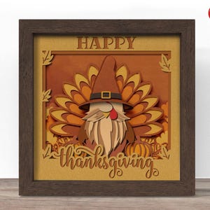 May include: A framed, layered paper art piece with a Thanksgiving theme. The artwork features a gnome dressed as a turkey, with the words "HAPPY thanksgiving" in a decorative font. The color palette includes shades of brown, orange, and yellow.
