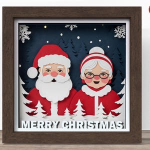 May include: A framed Christmas paper art piece depicting Santa and Mrs. Claus. The artwork has a layered design with a dark blue backdrop, white snowflakes, and the words "MERRY CHRISTMAS". The frame is a dark brown colour.