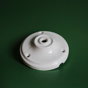 Puede incluir: Plafón de techo de cerámica blanca con tres agujeros y un agujero central para el cableado.