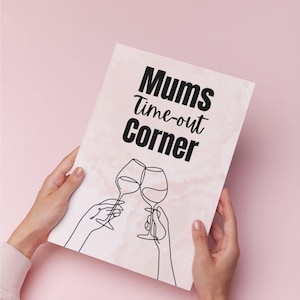 May include: A pink and white print with the text "Mums Time-out Corner" and a line drawing of two wine glasses clinking. The print is held by two hands against a pink background.