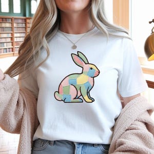 Peut inclure: T-shirt blanc avec un motif de lapin patchwork. Le lapin est composé de carrés aux couleurs pastel, rose, bleu, jaune et vert, soulignés de noir. Un vêtement décontracté pour tous les jours.
