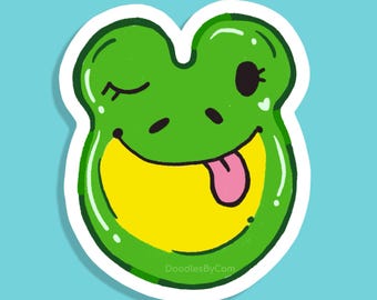 May include: A green frog sticker with a winking eye and a pink tongue sticking out. The frog has a yellow mouth and a white outline. The sticker is on a light blue background. The text "DoodlesByCom" is at the bottom.