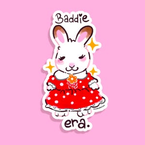 May include: A white bunny wearing a red dress with white polka dots and a flower on the collar. The bunny has brown ears and closed eyes. The text "Baddie era." is below the bunny.