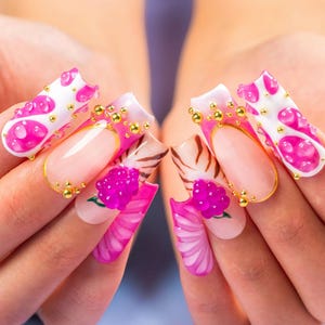 May include: A close-up of a set of long, decorated fingernails. The nails feature a variety of designs, including pink and white patterns, gold accents, and 3D floral embellishments. The overall aesthetic is vibrant and artistic.