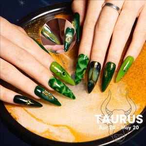 May include: A close-up of a set of long, pointed, green and gold nail designs. The nails feature various shades of green, gold accents, and a Taurus zodiac symbol. The image includes the text "TAURUS" and "Apr 20 - May 20".