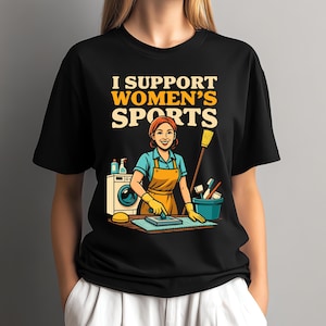 Peut inclure: T-shirt noir avec le texte "I Support Women's Sports" en jaune et blanc. Le graphisme représente une femme avec un tablier et des produits de nettoyage. Une machine à laver et un seau sont également dans l'image.
