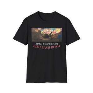 Puede incluir: Camiseta negra con un gráfico colorido de un mural y el texto rosa "BINGO BANGO BONGO BISH BASH BOSH". La camiseta es de cuello redondo.