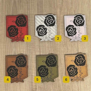 May include: Six colourful, shield-shaped patches with a black rose design. The patches are in red, white, pink, brown, olive green, and gold. Each patch is numbered from 1 to 6.