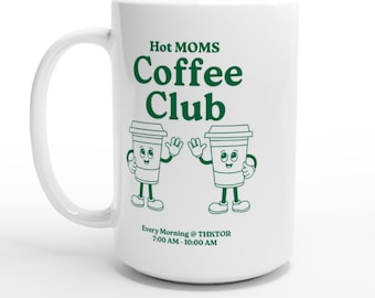 May include: White ceramic coffee mug with the text "Hot MOMS Coffee Club" in green. The mug features two cartoon coffee cups waving. The text "Every Morning @ THKTOR 7:00 AM - 10:00 AM" is also printed on the mug.