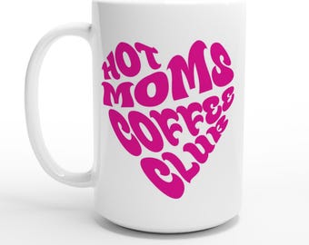 May include: White ceramic coffee mug with a large pink heart design. The heart contains the words "HOT MOMS COFFEE CLUB" in a retro, bubble font. The mug has a curved handle and is set against a white background.