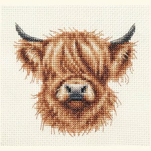 May include: Cross-stitch design of a Highland cow's head. The cow features long, shaggy brown fur, black horns, and a dark nose. The background is a cream-coloured fabric with a grid pattern.