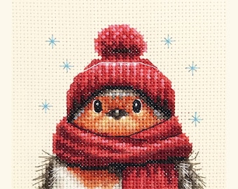 May include: Cross-stitch image of a bird wearing a red knit hat and scarf. The bird has a brown and orange body with black eyes and a black beak. The background is a light beige color with blue snowflake accents.