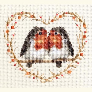 May include: Cross-stitch design featuring two robins on a branch, framed by a heart-shaped wreath. The birds have red breasts, white bellies, and grey and black wings. The wreath is made of brown twigs with red accents, set against a cream backdrop.