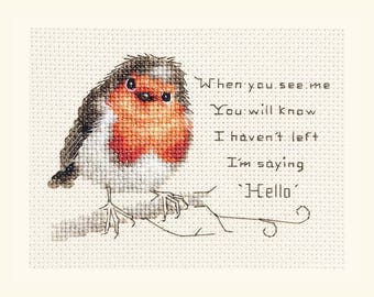 May include: Cross-stitch artwork featuring a detailed robin with a red breast, gray and black wings, and white accents. The text reads, "When you see me, you will know I haven't left, I'm saying 'Hello'." The bird is perched on a thin branch.