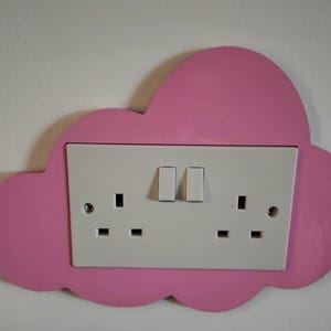 May include: A pink cloud-shaped wall plate with a white electrical socket and two light switches.