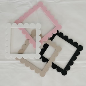 May include: Four decorative picture frames with scalloped edges. The frames are in pink, white, beige, and black.