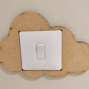 May include: A white light switch with a brown wooden cloud-shaped cover. The switch is in the off position.