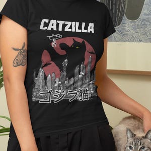May include: A black t-shirt with a graphic of a black cat in a Godzilla-like pose, with the text "CATZILLA" and Japanese characters that read "ゴジラ猫".