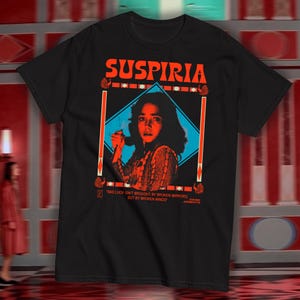 May include: Black t-shirt with a red and blue graphic of a woman with the text "Suspiria" and the quote "Bad luck isn't brought by broken mirrors, but by broken minds."