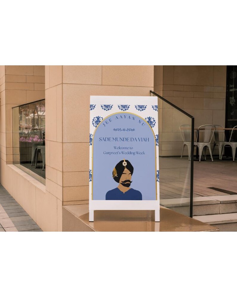 Op de afbeelding: Een wit bord met een blauw en gouden ontwerp. Het bord zegt "Jee Aayan Nu Sade Munde Da Viaah" en "Welkom bij Gurpreet's Wedding Week". Er is een cartoonillustratie van een man met een tulband.