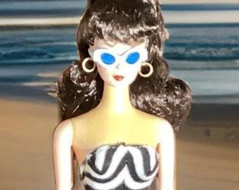 May include: A black and white striped swimsuit with a strapless design. The doll is wearing blue sunglasses and has dark brown hair.